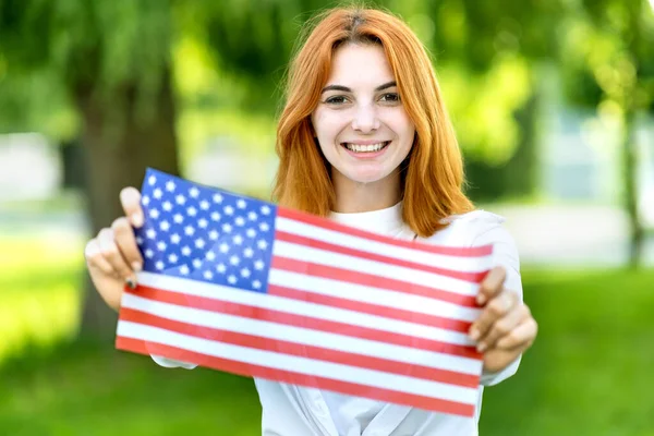 Szczęśliwa młoda kobieta pozowała z flagą USA na świeżym powietrzu w letnim parku. Ładna dziewczyna świętuje dzień niepodległości Stanów Zjednoczonych — Zdjęcie stockowe