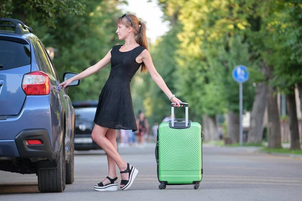 Glückliche junge Frau mit Koffertasche, die während einer Autofahrt neben ihrem Auto steht. Reise- und Urlaubskonzept — Stockfoto