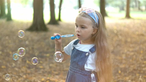 Pequeña niña feliz soplando burbujas de jabón al aire libre en el parque de verano —  Fotos de Stock
