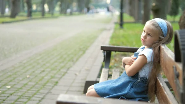 夏日公园里一个严肃的小女孩一个人坐在长椅上 — 图库照片