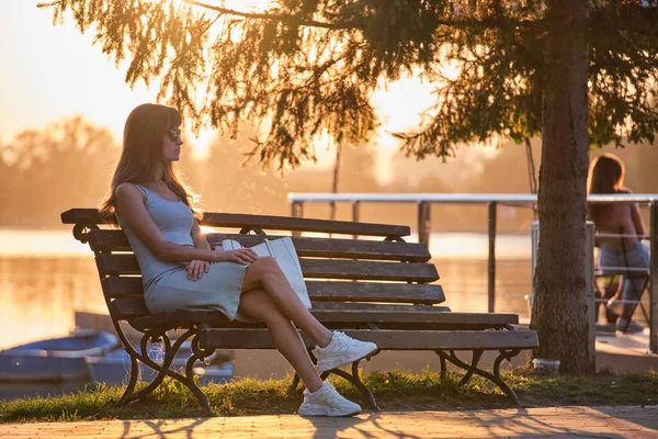 Eine einsame Frau sitzt auf einer Bank am See und genießt den warmen Sommerabend. Konzept für Einsamkeit und Entspannung — Stockfoto