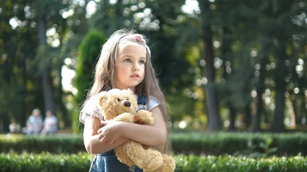 Niña bonita jugando con su juguete de oso de peluche favorito al aire libre en el parque de verano —  Fotos de Stock