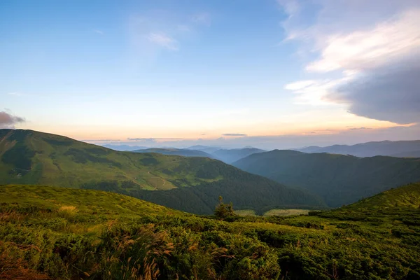 Sommerabend Berglandschaft mit grasbewachsenen Hügeln und fernen Gipfeln bei buntem Sonnenuntergang — Stockfoto