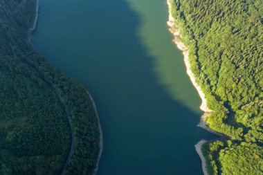 Yoğun yeşil ormanlarla kaplı yüksek dağ tepeleri arasında berrak mavi suyu olan büyük göl tepeden aşağıya doğru.