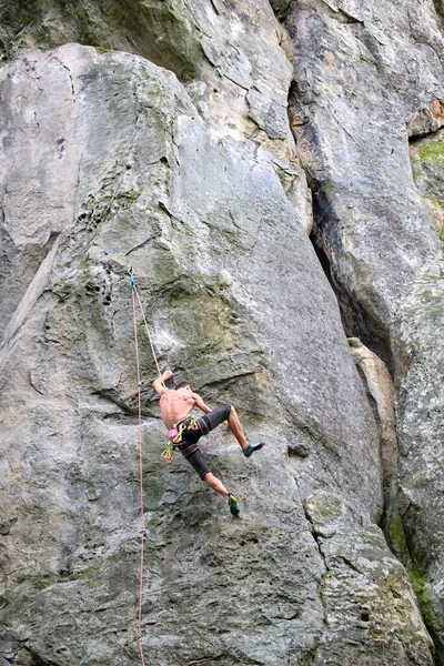 Young man climbing steep wall of rocky mountain. Male climber overcomes challenging route. Engaging in extreme sport concept — Stock Photo, Image