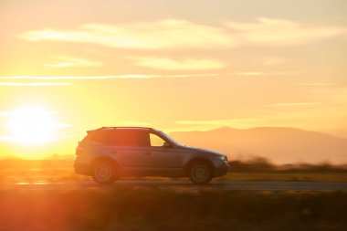 Gün batımında şehirlerarası yolda hızla giden bir SUV arabası. Akşamları otoyol trafiği