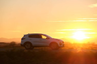 Gün batımında şehirlerarası yolda hızla giden bir SUV arabası. Akşamları otoyol trafiği