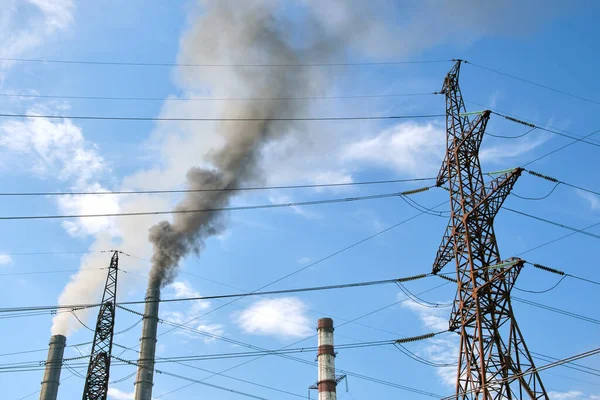 Högspänningsledningar mot kolkraftverk med höga rör med svart rök som rör sig uppåt förorenande atmosfär. Produktion av elenergi med fossila bränslen — Stockfoto