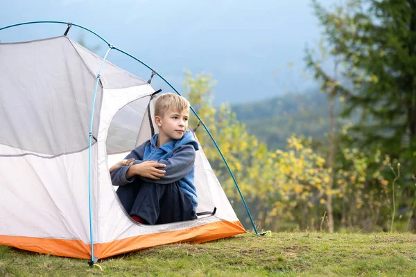 Senderista niño descansando sentado en una tienda de campaña en el camping de montaña disfrutando de la vista de la naturaleza de verano —  Fotos de Stock