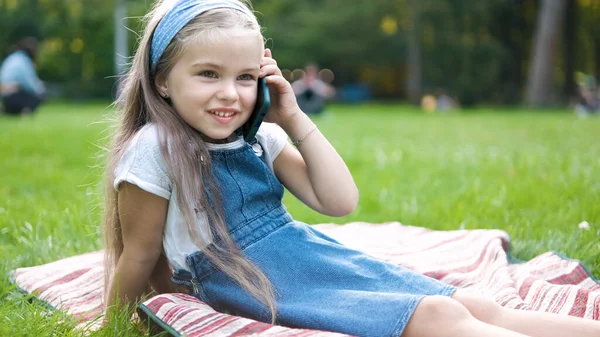 Söt liten flicka som har samtal på sin mobiltelefon i sommarparken — Stockfoto