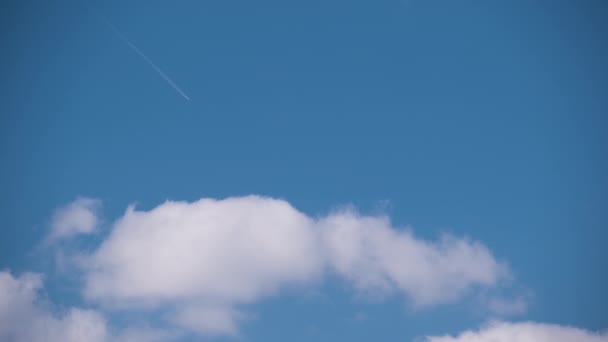 Aereo a reazione passeggeri distanti che vola in alta quota sul cielo blu con nuvole bianche lasciando tracce di fumo di contrail dietro. Concetto di viaggio aereo — Video Stock