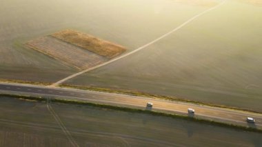 Gün batımında hızlı giden arabalarla şehirlerarası yol manzarası. Akşamları otoban trafiğinin insansız hava aracı görüntüsü