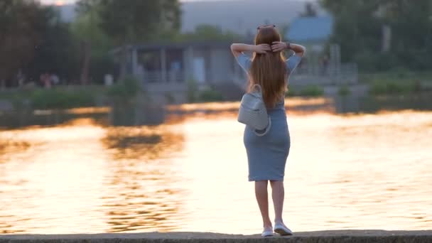 Baksidan av ensam kvinna står på sjön sida på varm kväll. Ensamhet och avslappning koncept — Stockvideo