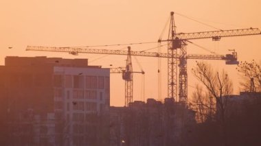 Gün batımında yüksek apartmanlı inşaat alanındaki vinçlerin koyu renkli silueti. Gayrimenkul geliştirme