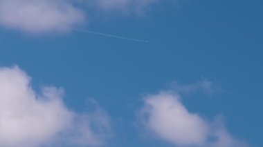 Uzaktaki yolcu uçağı mavi gökyüzünde yüksek irtifada uçarken beyaz bulutlar ardında iz bırakıyor. Hava yolculuğu konsepti