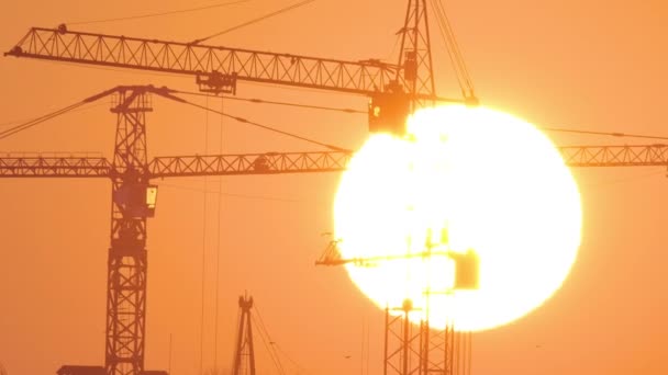 Silueta oscura de grúas torre con gran puesta de sol en edificios de apartamentos residenciales de alto sitio de construcción al atardecer. Desarrollo inmobiliario — Vídeo de stock