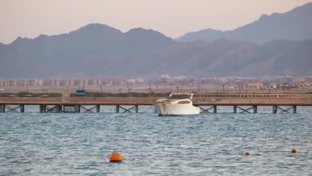 Paysage marin avec surface ondulée d'eau de mer bleue avec yacht lointain à l'extrémité de la jetée longue flottant sur des vagues calmes — Video