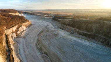 Kazı makineleri ve çöp kamyonlarıyla inşaat endüstrisi için kumtaşı malzemelerinden oluşan açık maden manzarası. Madencilik ve kullanışlı mineral üretiminde ağır ekipman
