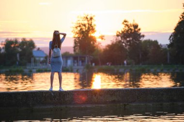 Gölün kıyısında tek başına duran ve sıcak akşamın tadını çıkaran yalnız bir genç kadın. Doğada refah ve rahatlama kavramı