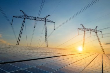 Elektrik hatları olan yüksek voltaj kuleleri günbatımında güneş fotovoltaik panellerinden enerji aktarıyor. Sürdürülebilir elektrik üretimi