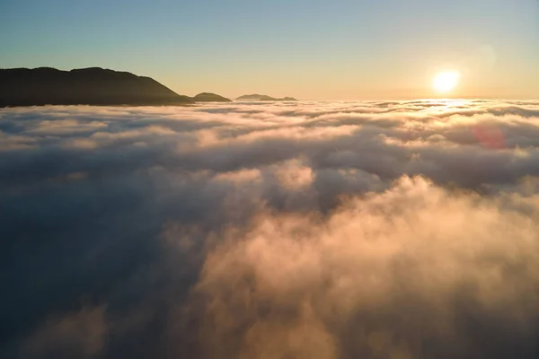 Vista aérea del colorido amanecer sobre la densa niebla blanca con siluetas oscuras distantes de colinas de montaña en el horizonte —  Fotos de Stock