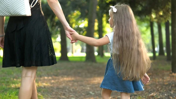 Back view of mother and her little daughter child walking together holding hands in summer park — Stock Photo, Image