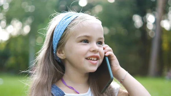 Mooi klein kind meisje hebben gesprek op haar mobiele telefoon in de zomer park — Stockfoto