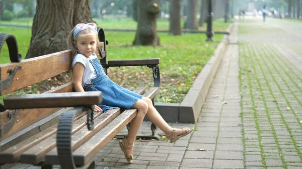 Küçük mutlu bir kız çocuğu yaz parkında bir bankta dinleniyor. — Stok fotoğraf