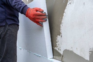 İnşaat işçisi termal koruma için evin ön cephesine köpük yalıtım çarşafları yerleştiriyor.