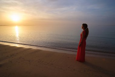Genç bir kadın okyanus kumsalında tek başına sıcak tropikal bir akşamın tadını çıkarıyor.