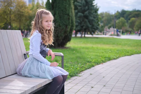Porträtt av söt barn flicka sitter på parkbänk utomhus — Stockfoto