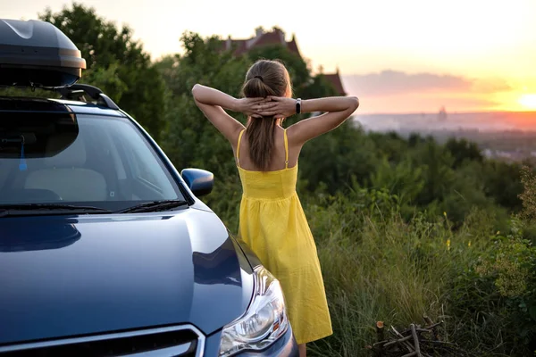 Yong mujer feliz de pie cerca de su coche disfrutando de la puesta del sol vista de la naturaleza del verano. Concepto de viaje y escapada — Foto de Stock