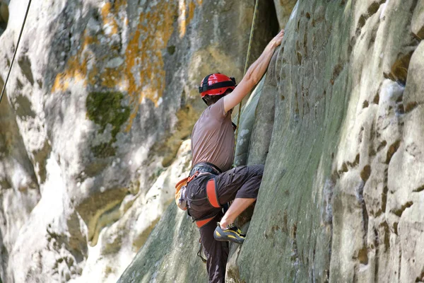 Young man climbing steep wall of rocky mountain. Male climber overcomes challenging route. Engaging in extreme sport concept — Stock Photo, Image