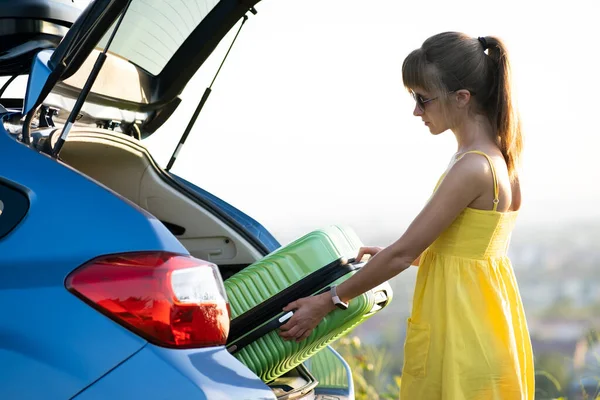 Mujer joven tomando la maleta verde del maletero del coche. Concepto de viajes y vacaciones — Foto de Stock