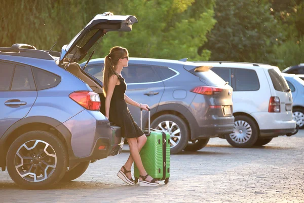 Junge Frau mit Koffertasche wartet neben Auto. Reise- und Urlaubskonzept — Stockfoto