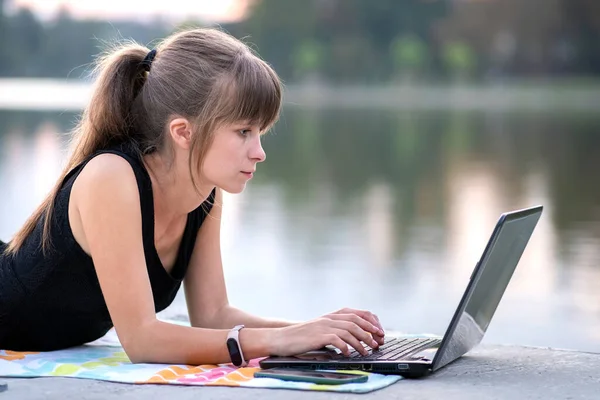 Mujer joven que trabaja detrás de la computadora portátil acostado en el parque de verano al aire libre — Foto de Stock