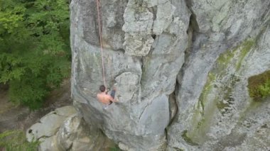 Genç adam kayalık dağın dik duvarından aşağı iniyor. Erkek tırmanışçı zorlu rotayı aşar. Ekstrem spor konseptine dalmak