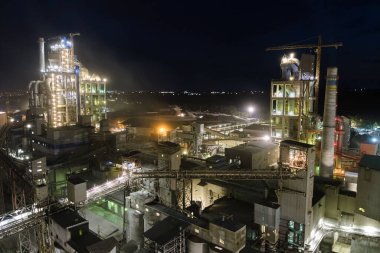 Yüksek beton yapılı çimento fabrikası ve endüstriyel üretim alanında geceleri kule vinçleri. Üretim ve küresel sanayi kavramı