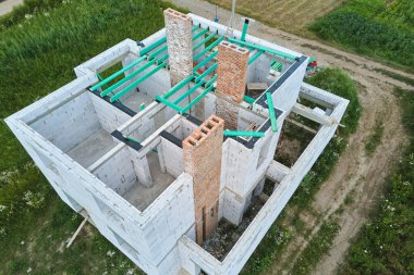 Havalandırılmış hafif beton duvarları ve inşaat halindeki ahşap çatı kirişleri olan bitmemiş özel evin havadan görüntüsü.