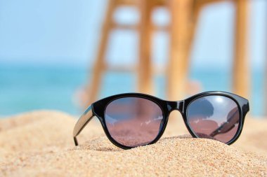 Sıcak güneşli bir günde, tropikal deniz kıyısındaki kumlu sahilde siyah koruyucu güneş gözlüğü. Yaz tatili kavramı