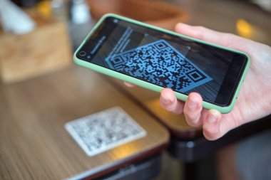 Konuk elin restoranda yemek sipariş ederken çevrimiçi menü için qr kodunu cep telefonuyla taraması