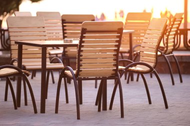 Şehir caddesinde gün batımında açık kafe sandalyeleri ve masa kapanıyor.