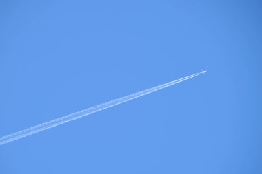 Mesafeli yolcu jet uçağı açık mavi gökyüzünde yüksek irtifada uçarken ardında beyaz duman izi bırakıyor. Hava taşımacılığı kavramı