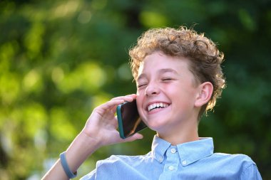 Yazlık parkta cep telefonuyla konuşan mutlu genç bir çocuk. Çevrimiçi arkadaşlık kavramı