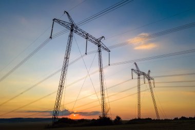 Gün batımında elektrik hatları olan yüksek voltaj kuleleri.
