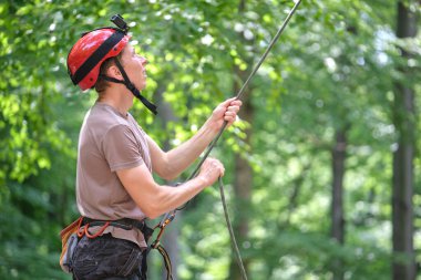 Adam bağlanma cihazı ve iple ortağını bağlıyor. Tırmanışçılar kaya dağcılığı güvenliği için ekipman tutuyor.