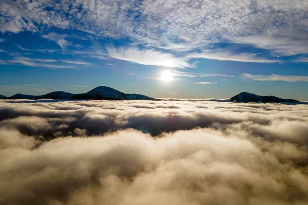 Aerial view of vibrant sunrise over white dense clouds with distant dark mountains on horizon — Stock Photo, Image