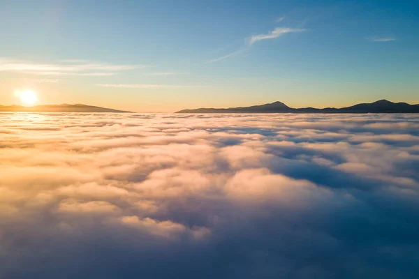 Vista aérea del vibrante amanecer amarillo sobre densas nubes blancas y montañas distantes en el horizonte —  Fotos de Stock