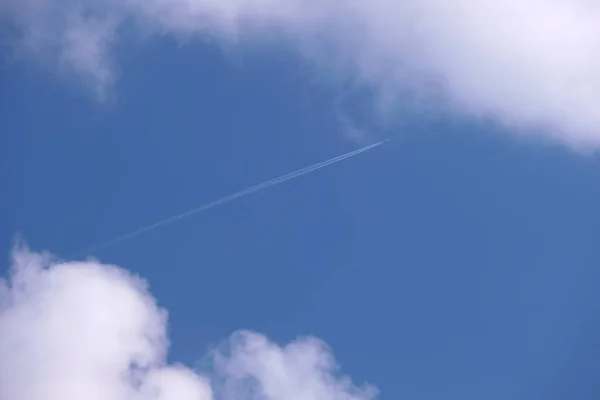 Uzaktaki yolcu uçağı mavi gökyüzünde yüksek irtifada uçarken beyaz bulutlar ardında iz bırakıyor. Hava yolculuğu konsepti — Stok fotoğraf