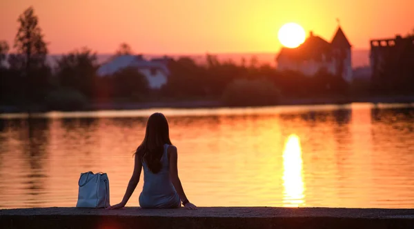외로운 여자가 따뜻 한 저녁에 홀로 호수 가에 앉아 있습니다. 자연의 개념 에서의 고독 과 긴장 — 스톡 사진